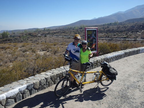 Terry and Dennis Struck posing with the Bee (tandem bicycle) in front of the road turnoff for the Ampimpa Observatory, Argentina.